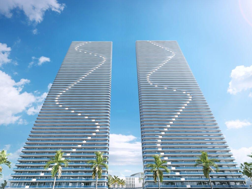 Twin towers of Aria Reserve Residences with unique wave-like designs on the facades, set against a clear evening sky with palm trees in the foreground.