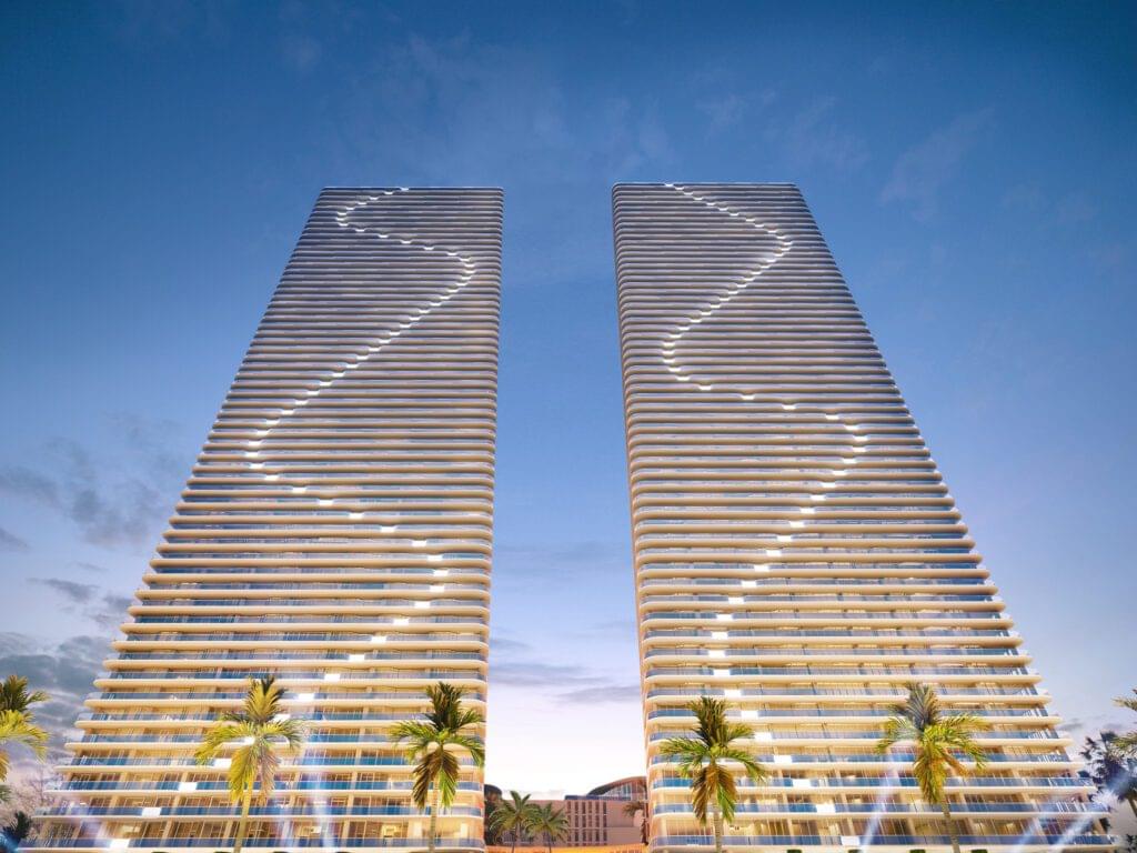 Twin towers of Aria Reserve Residences with unique wave-like designs on the facades, set against a clear evening sky with palm trees in the foreground.